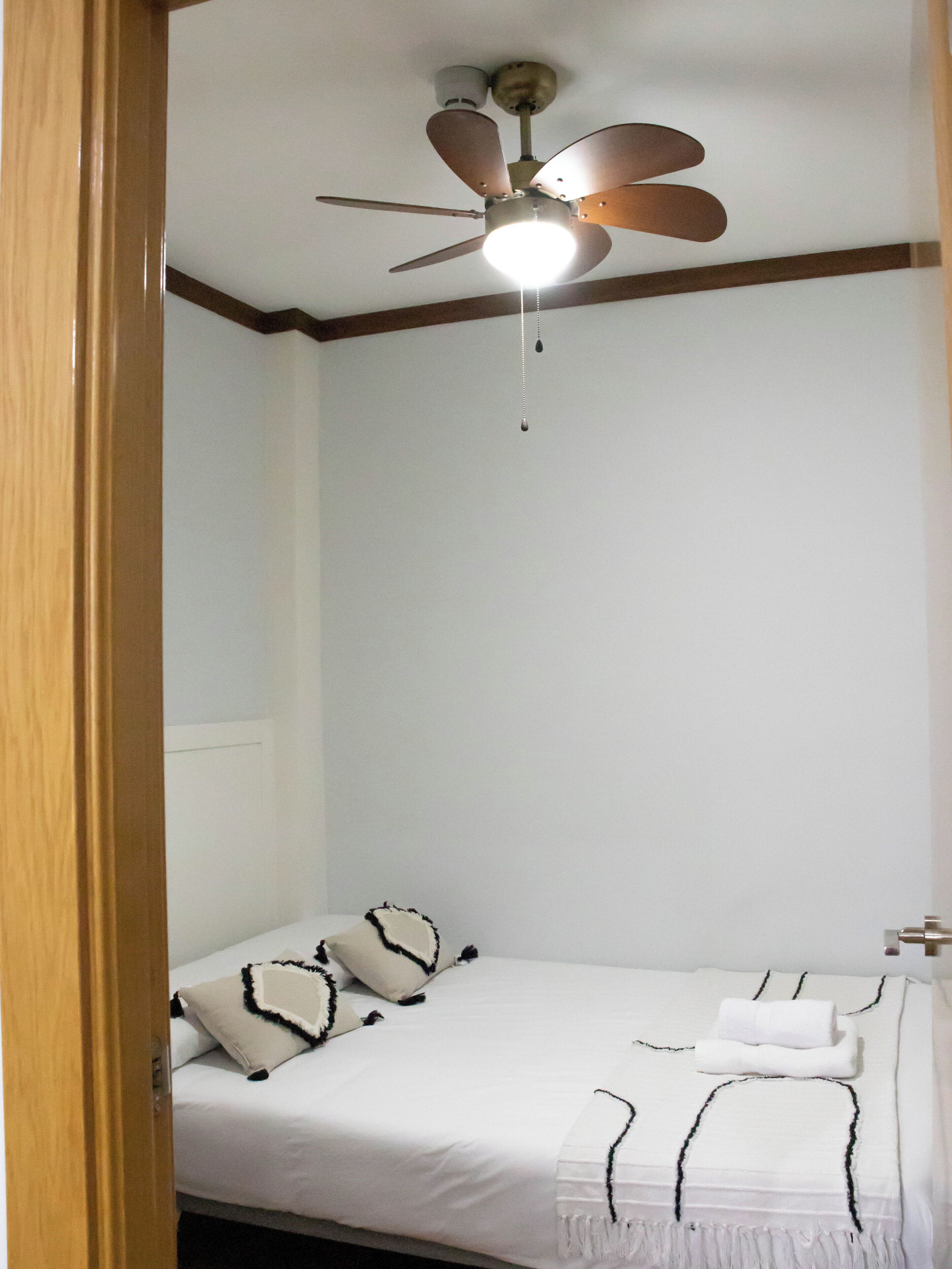 Habitación de hotel con una cama individual, ventilador de techo y pared blanca.