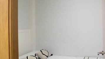 Habitación de hotel con una cama individual, ventilador de techo y pared blanca.