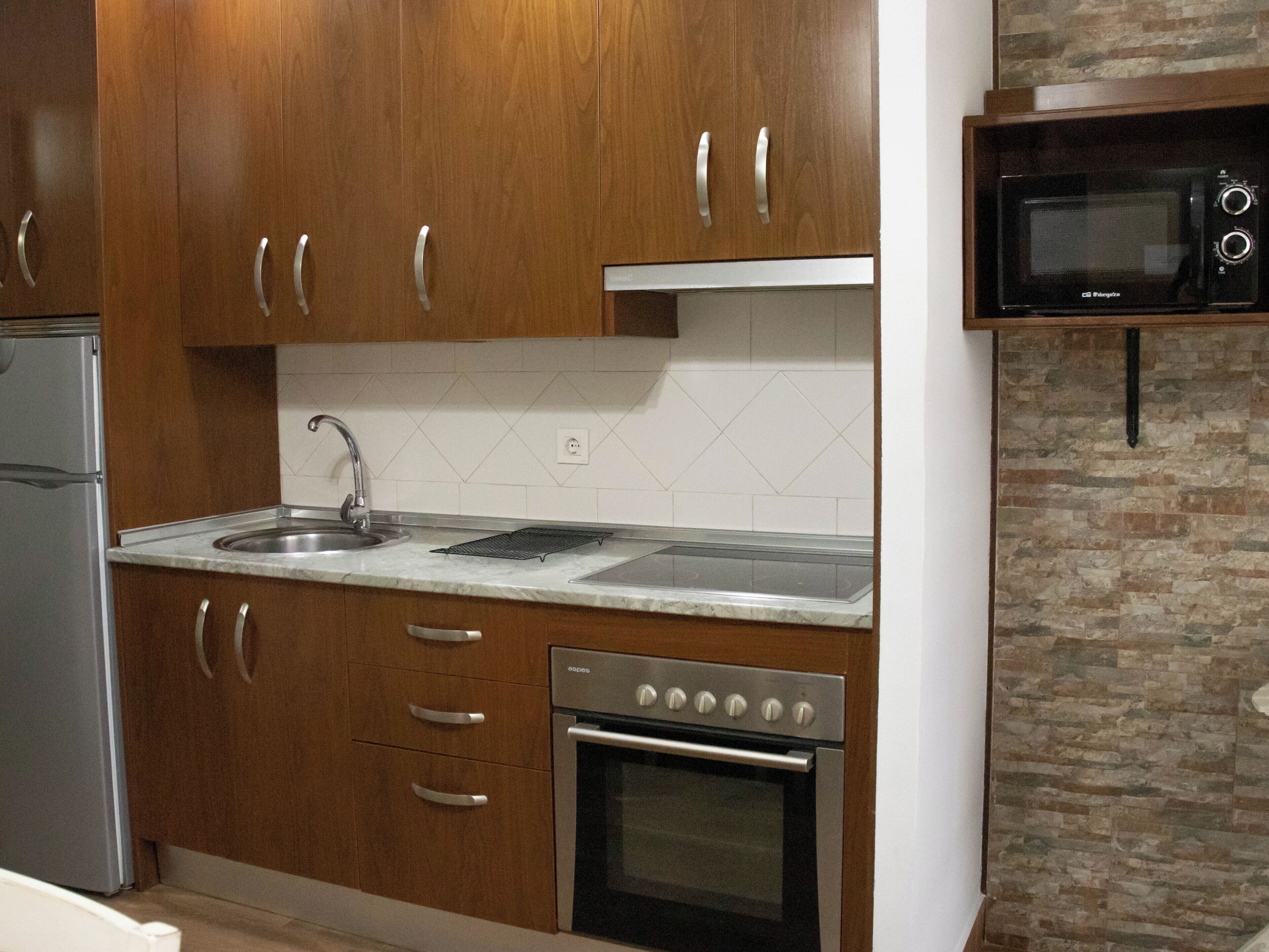 Una cocina con armarios de madera, un lavamanos de acero inoxidable, un microondas integrado y un horno.
