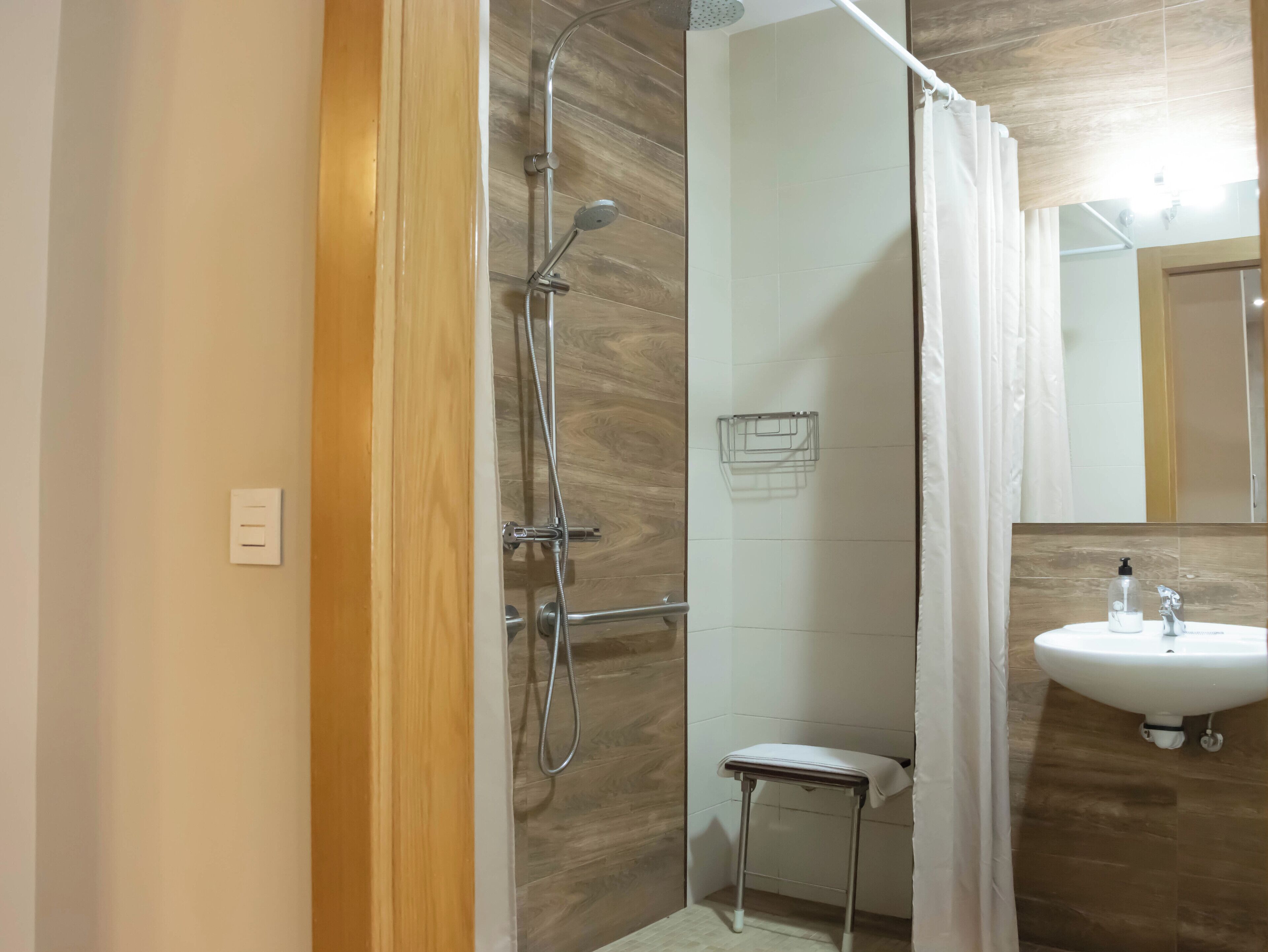 A modern bathroom with a shower, a small stool, and a sink with a mirror.
