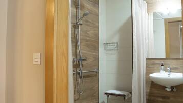 A modern bathroom with a shower, a small stool, and a sink with a mirror.