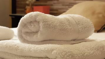 A neatly folded white towel stacked on a bed with a textured white and black blanket.