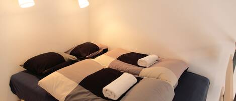 Una cama doble con colcha azul oscuro y color crema, dos lámparas de pared y suelo de madera.