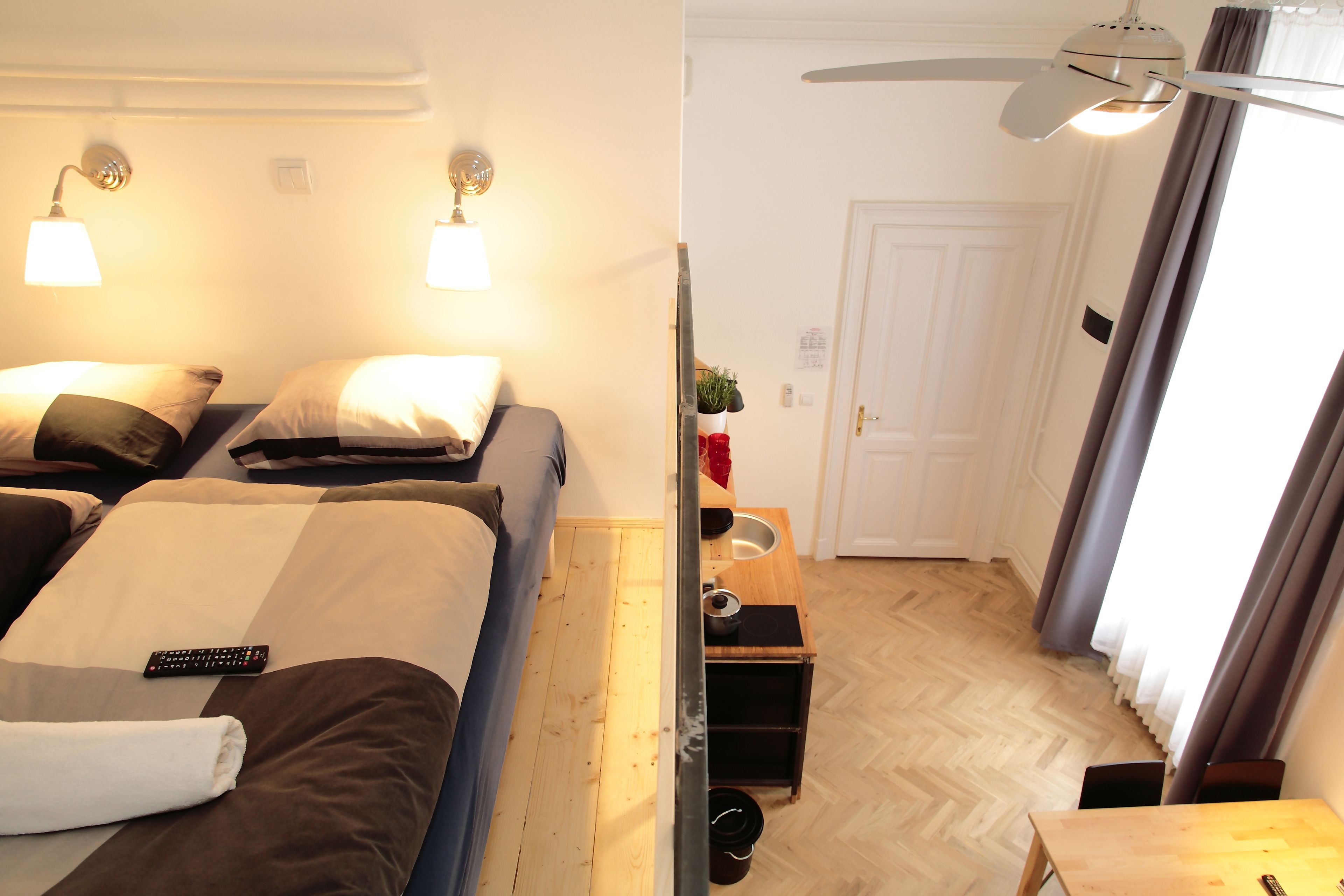 A hotel room with a bed, bedside lamps, a small table with a plant, and a door.