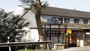 Un hotel llamado "HOTEL ARTXANDA" con un letrero, una entrada porticada y un muro de piedra.