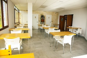 A classroom with wooden desks and white chairs, a bookshelf, and two doors. - Hotel Artxanda (Bilbao)