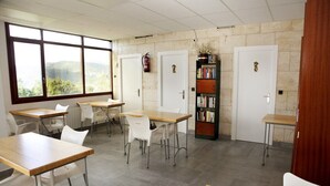Un aula con mesas y sillas, una estantería y un extintor.