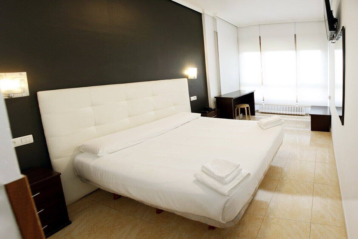 Quarto de hotel moderno com uma cama grande, uma escrivaninha pequena, uma cadeira e um radiador.