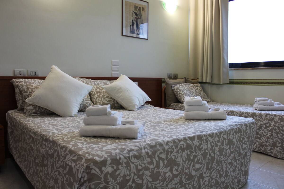 A hotel room with two beds, each with a patterned bedspread and pillows, and neatly folded towels on the beds.