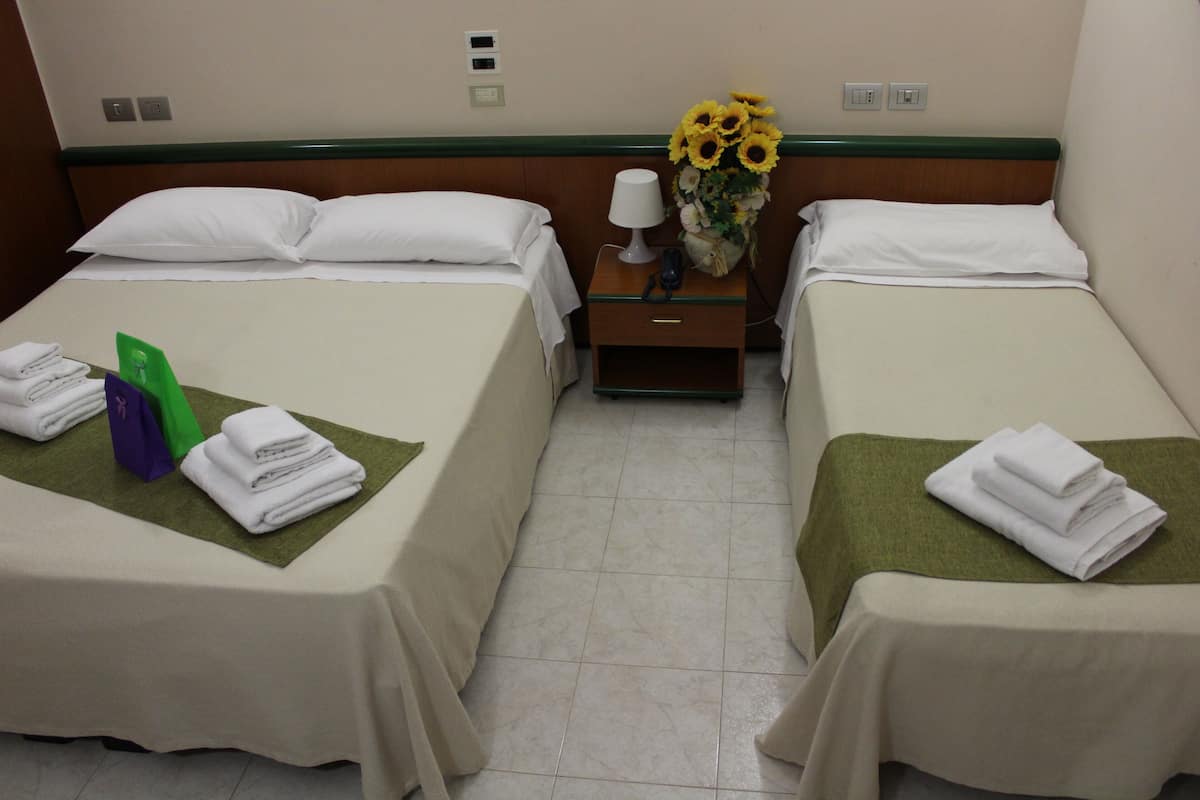 A hotel room with two beds, a nightstand with a lamp and a vase of sunflowers, and towels on the beds.