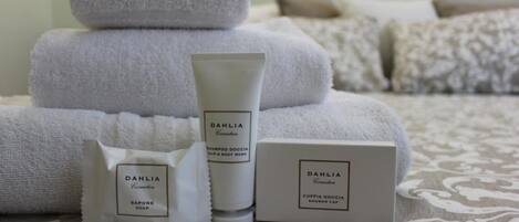 Un ensemble de produits de toilette soigneusement disposé, comprenant un savon, un flacon de shampoing et un bonnet de douche, le tout de la marque Dalia Cosmetics, placé sur une couvre-lit à motifs.