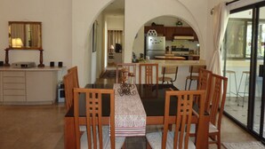 A dining area with a table and chairs, an arched doorway leading to a kitchen, and a view through a glass door. - Casa Sun Guadalupe (San José del Cabo)