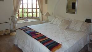 A bedroom with a large bed, a window with curtains, a bedside lamp, and a wall-mounted mirror. - Casa Sun Guadalupe (San José del Cabo)