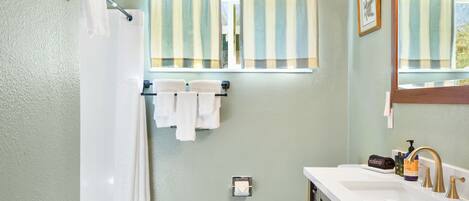 Un bagno con pavimento in legno, un WC bianco, un lavandino bianco con specchio e tende veneziane a righe.