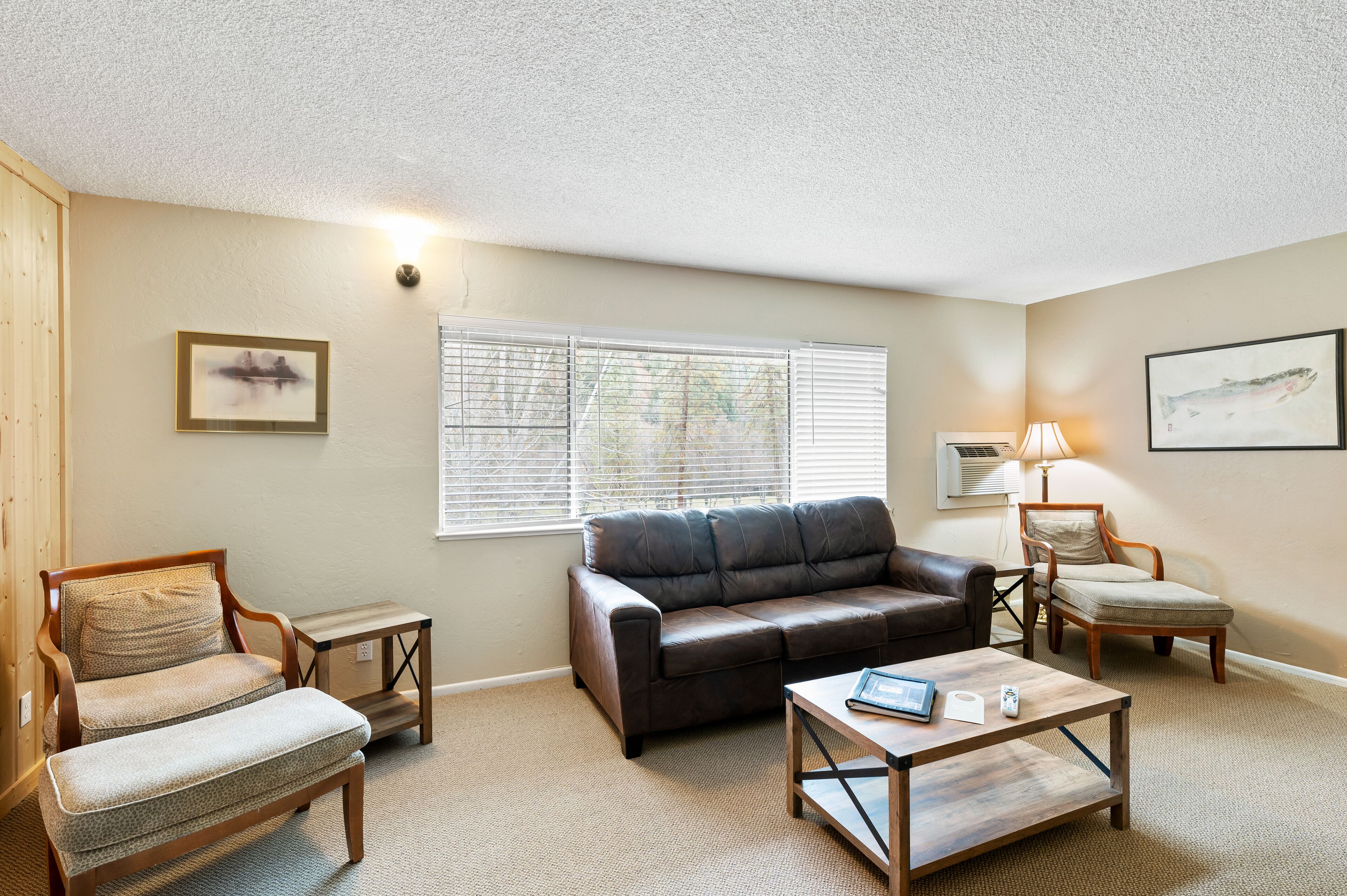 A living room with a brown leather sofa, two wooden chairs, a coffee table, and a window with blinds.