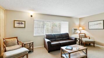 A living room with a brown leather sofa, two wooden chairs, a coffee table, and a window with blinds.