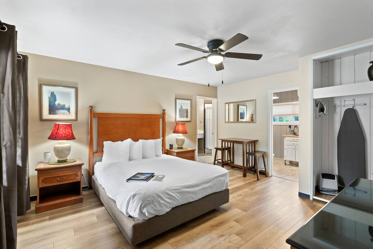 Une chambre d’hôtel comprenant un lit, deux tables de chevet avec lampes, un ventilateur de plafond, un bureau et un coin cuisine.
