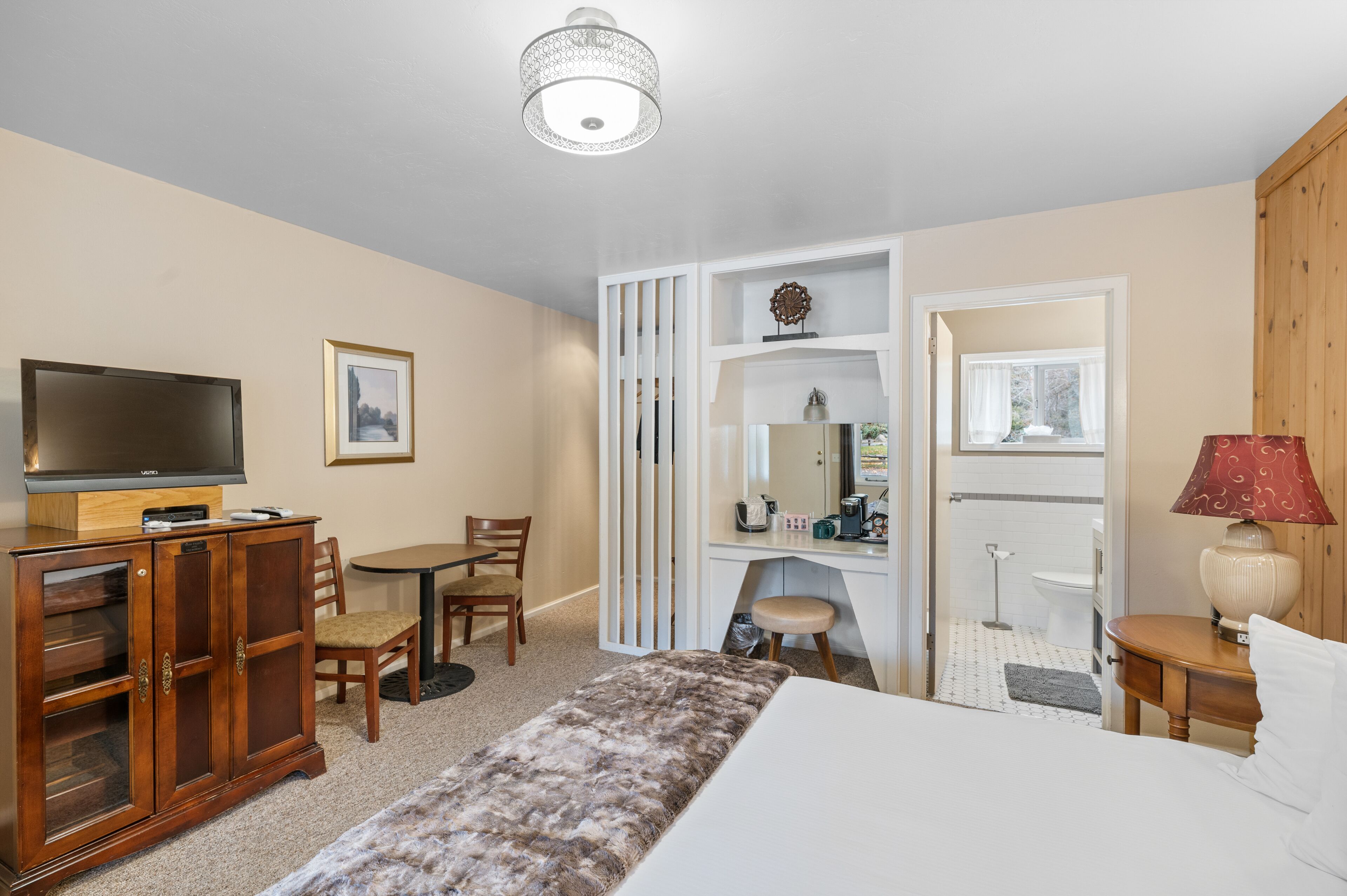 A hotel room with a bed, a TV, a desk, a chair, a wardrobe, and a bathroom visible through an open door.