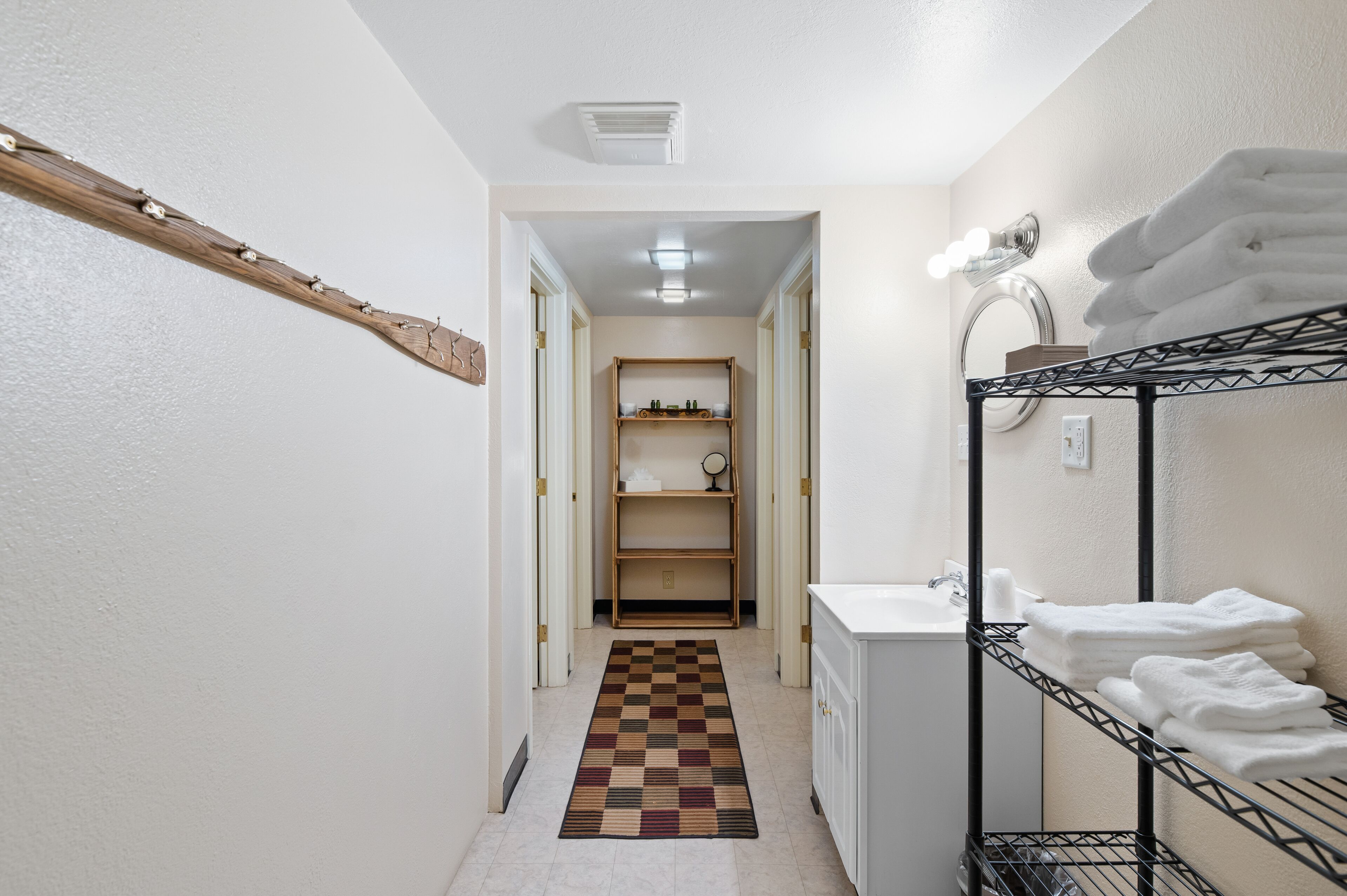 Un pasillo estrecho con un alfombra a cuadros, un estante de madera, un lavabo y un perchero.