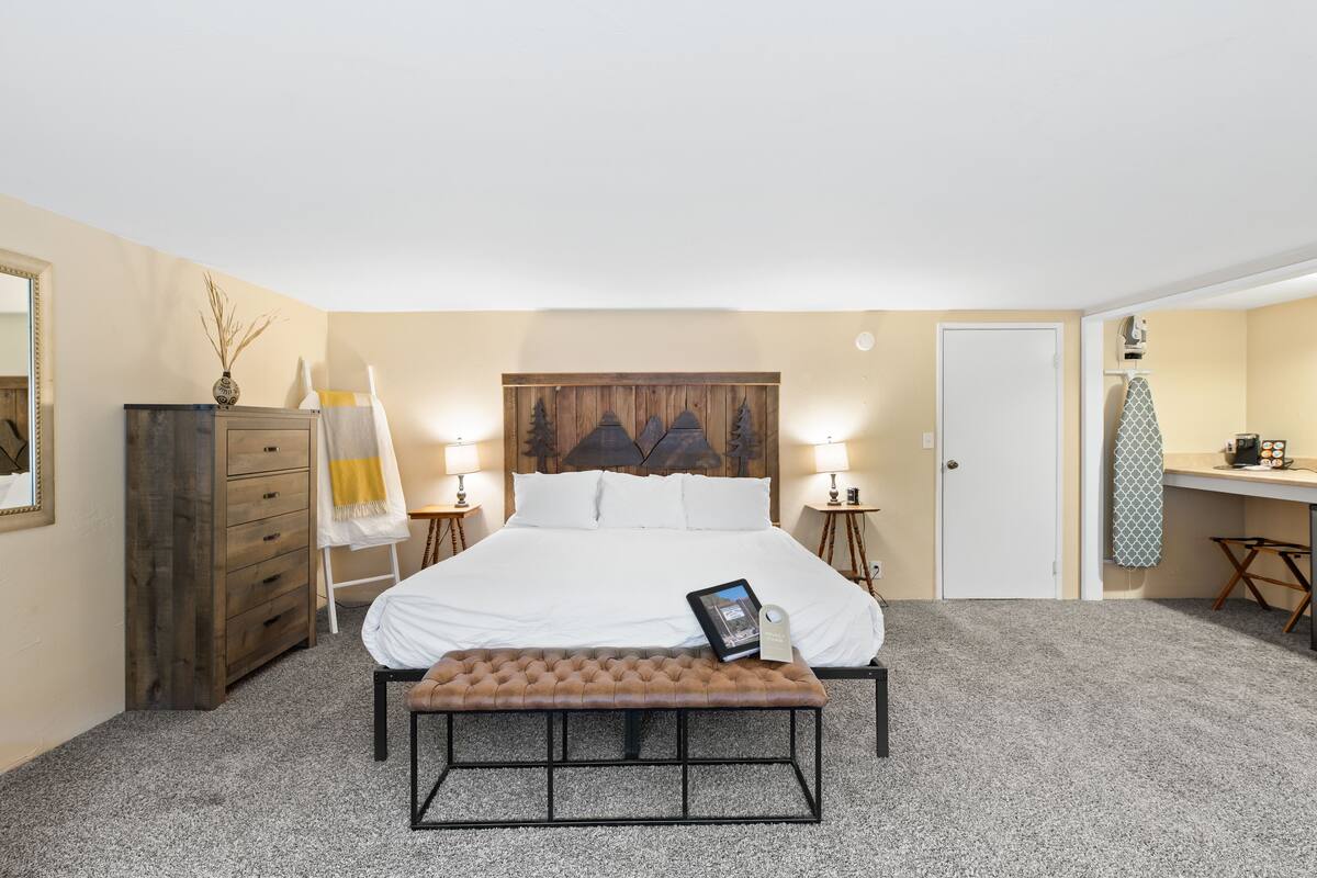 Une chambre à coucher comprenant un lit, des tables de chevet, un bureau, une chaise, un banc, une commode et une porte.