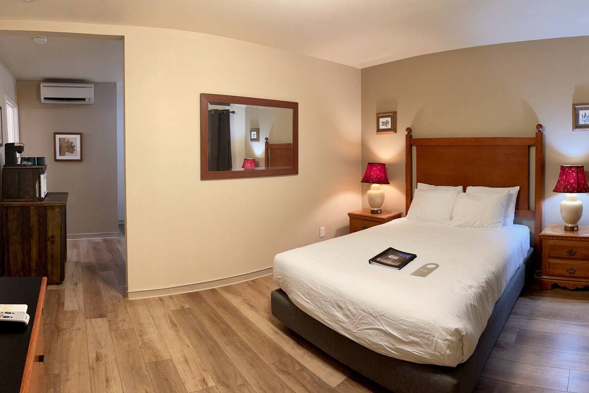 Une chambre à coucher bien rangée, avec un lit, des lampes de chevet, une table de nuit, une commode en bois et un miroir au mur.