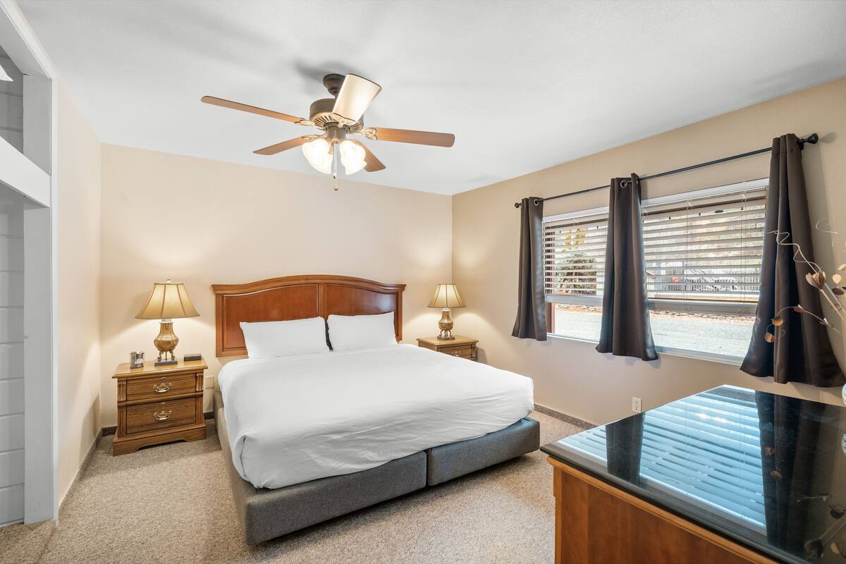 Une chambre d’hôtel avec un lit, deux tables de chevet avec des lampes, un ventilateur de plafond, une fenêtre avec des rideaux et une vue sur l’extérieur.