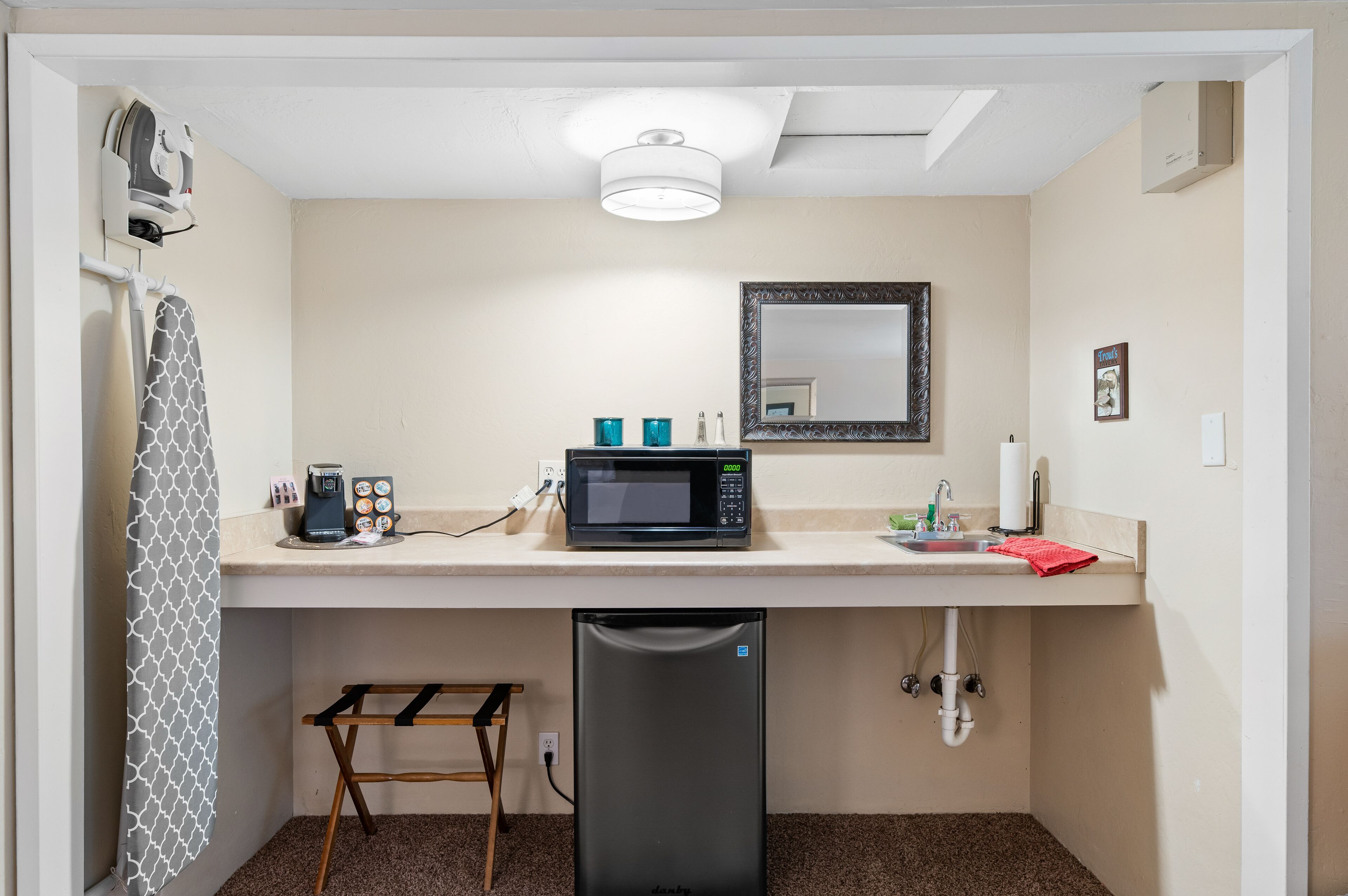 Una kitchenette compacta con microondas, cafetera y un refrigerador pequeño.