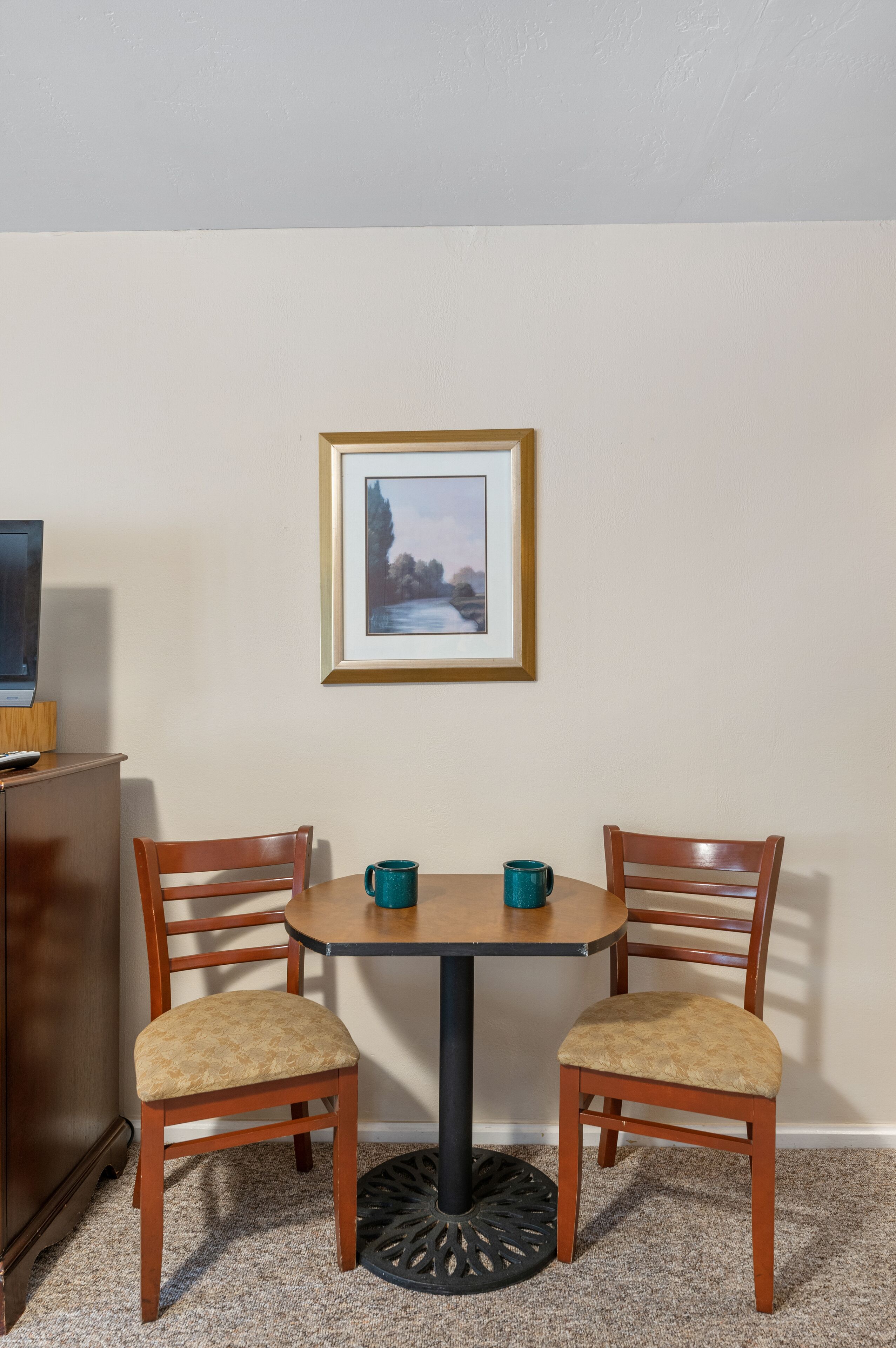 Ein kleiner Essbereich mit einem runden Tisch, zwei Holzstühlen und einem gerahmten Bild an der Wand.