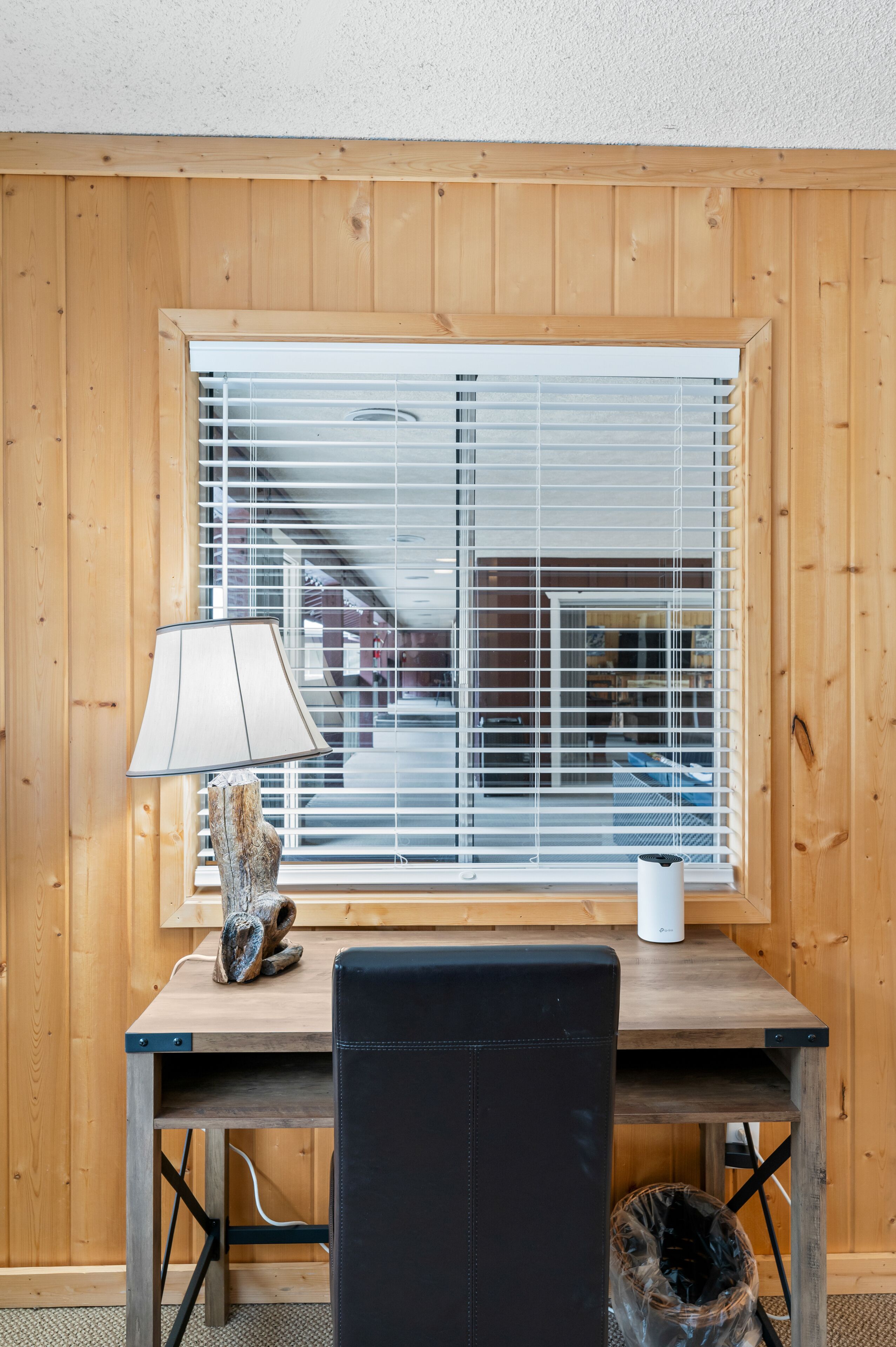 Una habitación con paneles de madera, un escritorio, una lámpara y una ventana con persianas.