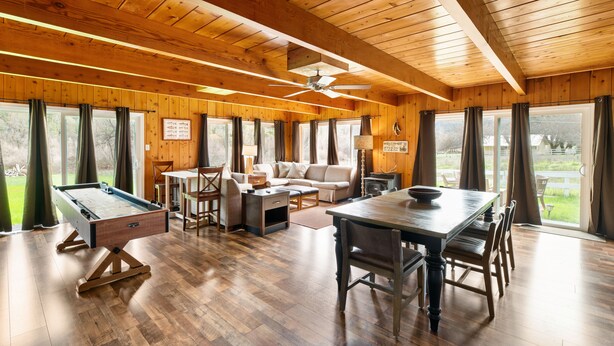 Ein Holzinterieur mit Billardtisch, Sofa, Esstisch und großen Fenstern.