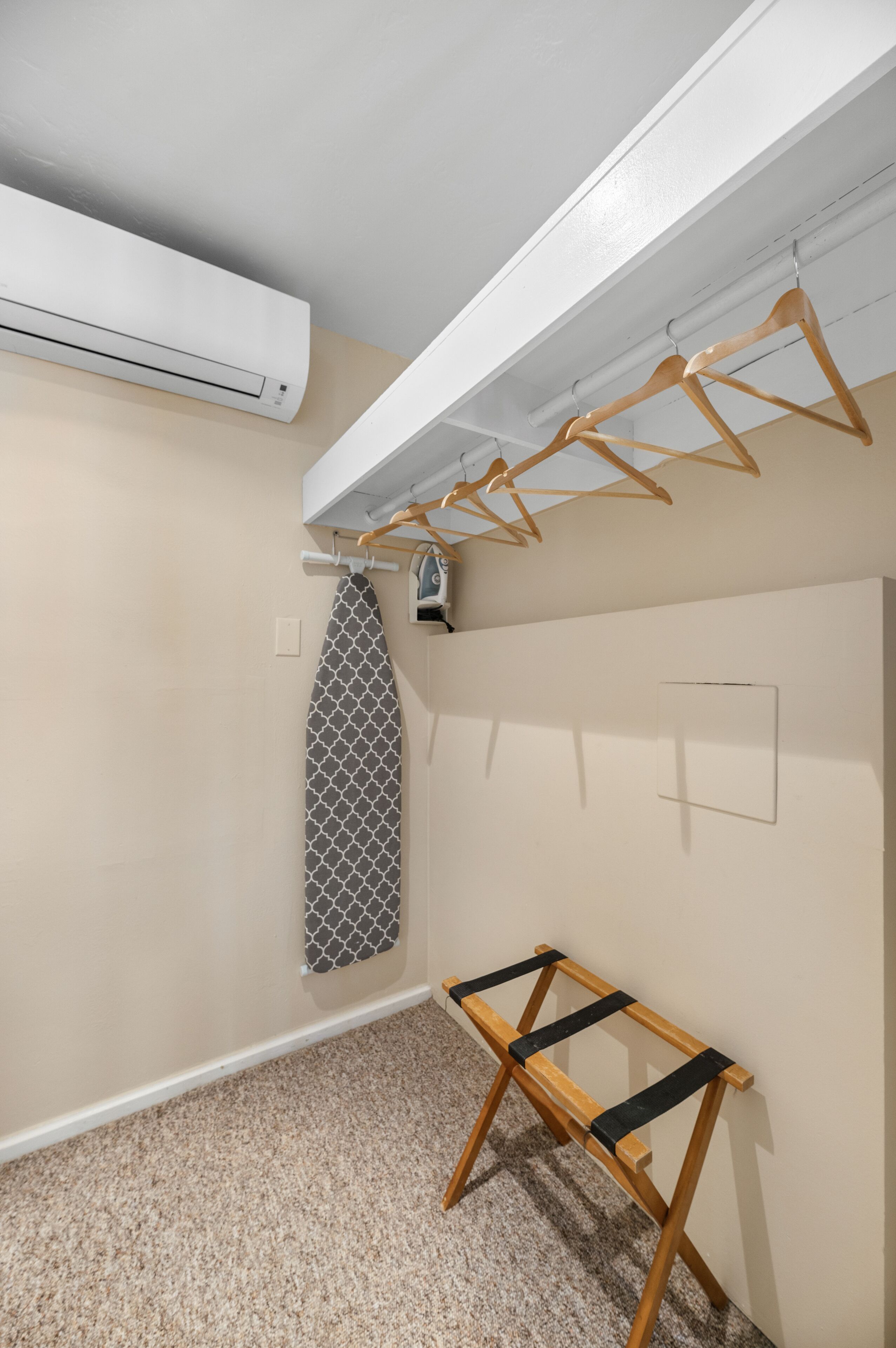 A room with a ceiling-mounted air conditioner, a wooden drying rack, a towel rack, and a small table.