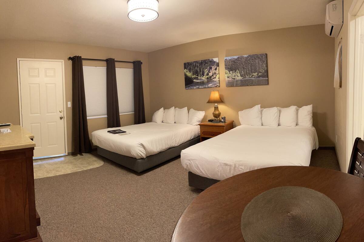 Une chambre d’hôtel avec deux lits, un bureau avec un ordinateur, une lampe et deux tableaux au mur.