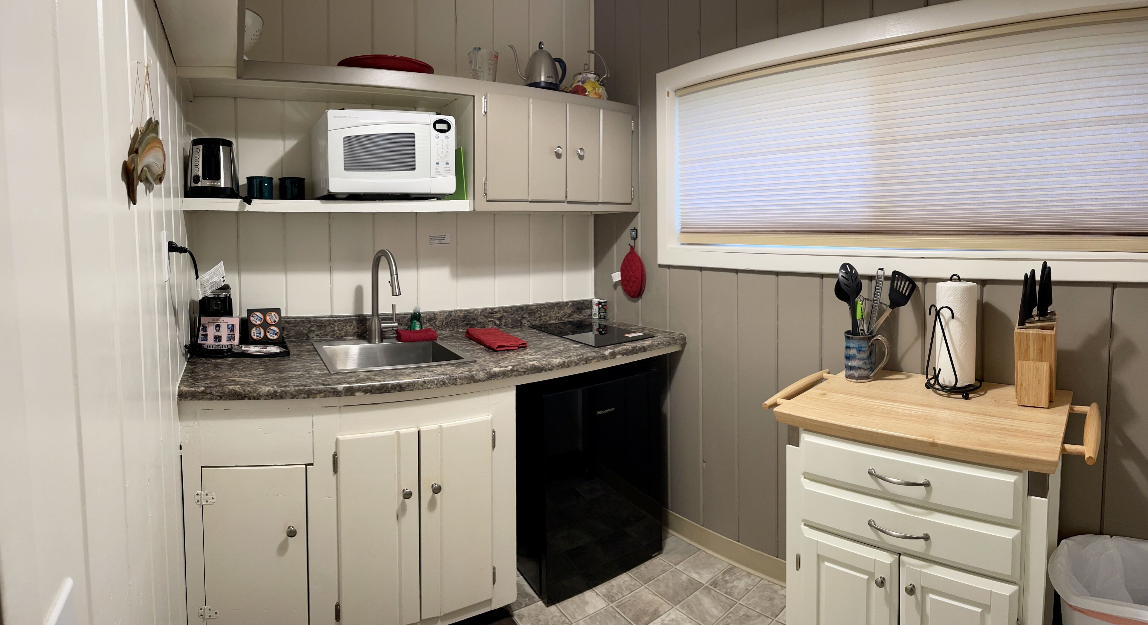 A compact kitchen with white cabinets, a microwave, a sink, and a wooden countertop.