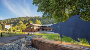 Eine Lodge mit einer großen Büffelskulptur davor, umgeben von felsigem Gelände und einem Holzzaun.