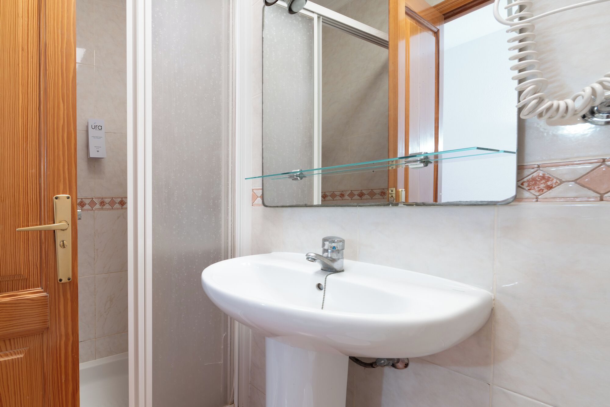 A bathroom with a white sink, a glass shelf, and a wooden door.