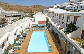 Una piscina al aire libre, sombrillas, sillones reclinables de piscina