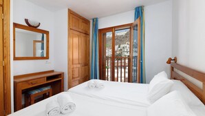 Habitación de hotel con cama, escritorio de madera, espejo y vistas a edificios por la ventana.