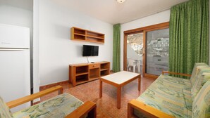 Un espacio habitable compacto con un sofá, un televisor, una mesita y un estante empotrado.