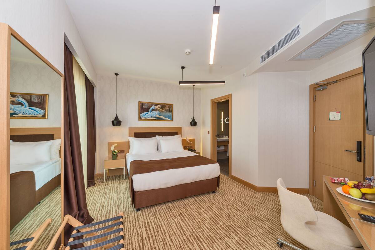 Ein Hotelzimmer mit einem großen Bett, einem Schreibtisch mit Obstschale, einem Fernseher und einem Spiegel.