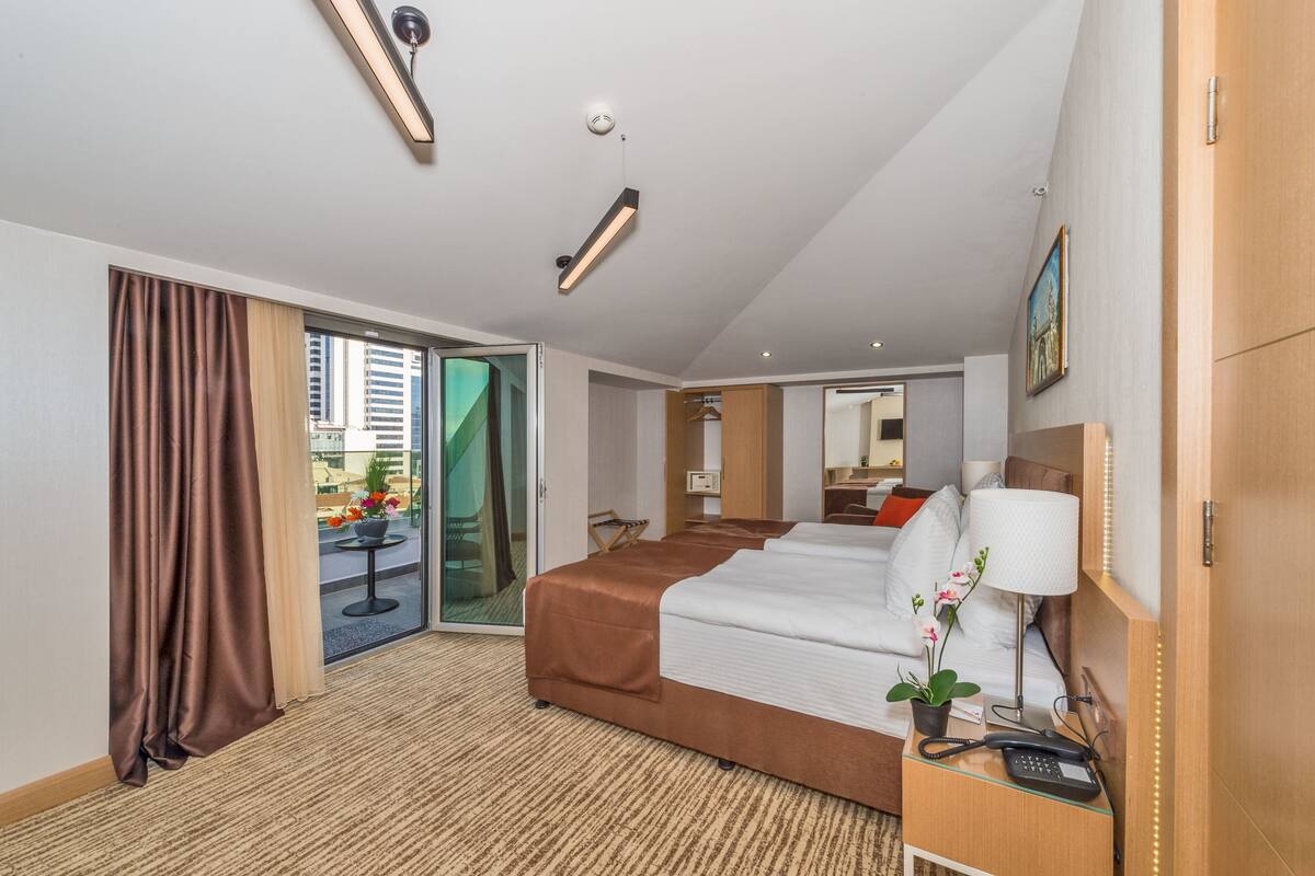 Ein Hotelzimmer mit einem großen Bett, einem Schreibtisch mit Lampe, einem Telefon und Blick auf die Stadt durch die Glasdoor.