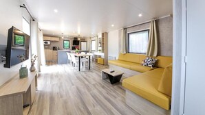 Una sala de estar moderna con un sofá amarillo, un televisor de pantalla plana y una zona de comedor con mesa y sillas.