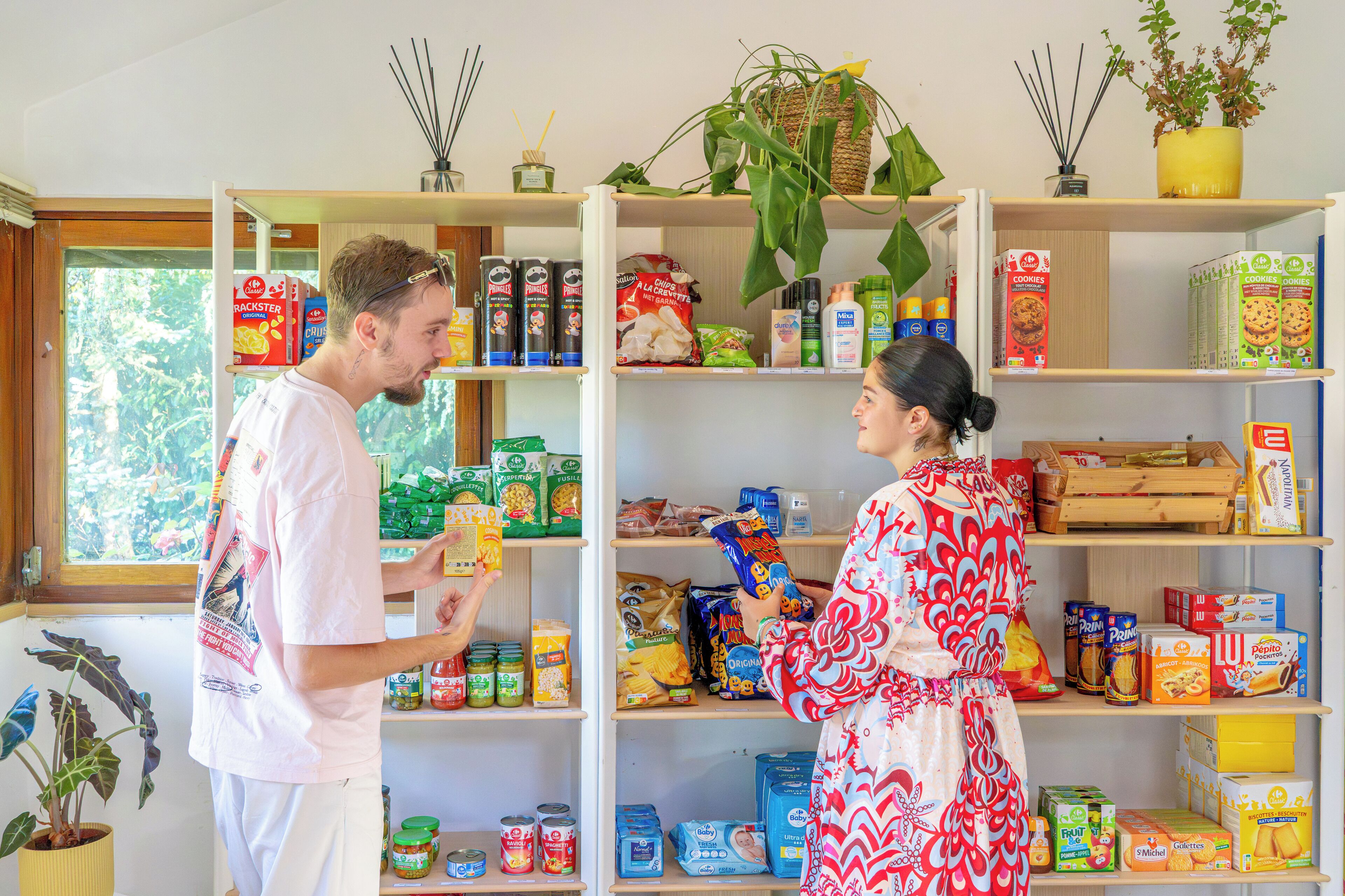Een keuken met planken vol diverse etenswaren en een raam met uitzicht op bomen.