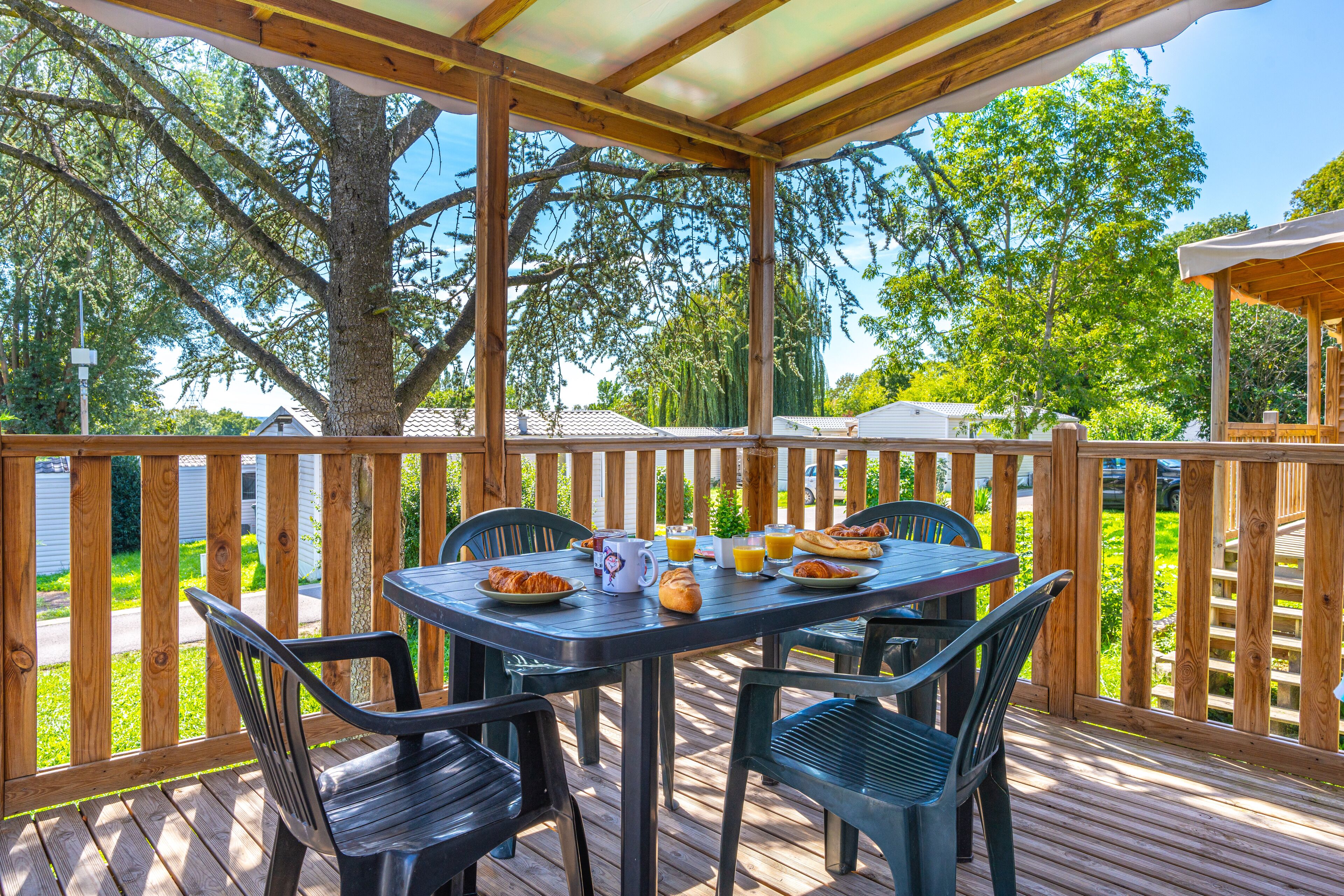 Terraza cubierta al aire libre con una mesa dispuesta para el desayuno, rodeada de sillas.