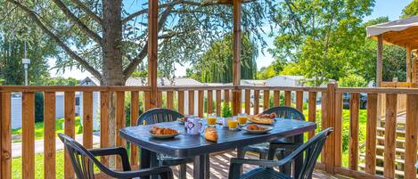 Terraza cubierta al aire libre con una mesa dispuesta para el desayuno, rodeada de sillas.
