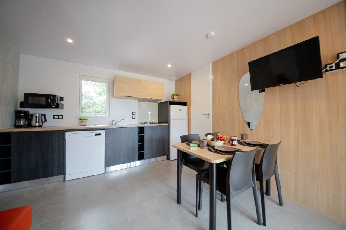 Una cocina moderna con comedor, que incluye una televisión de pantalla plana montada en la pared, microondas, cafetera y lavavajillas.