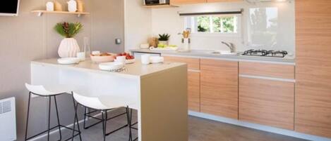 A modern kitchen with a central island, bar stools, wooden cabinets, a microwave, and a gas stove.