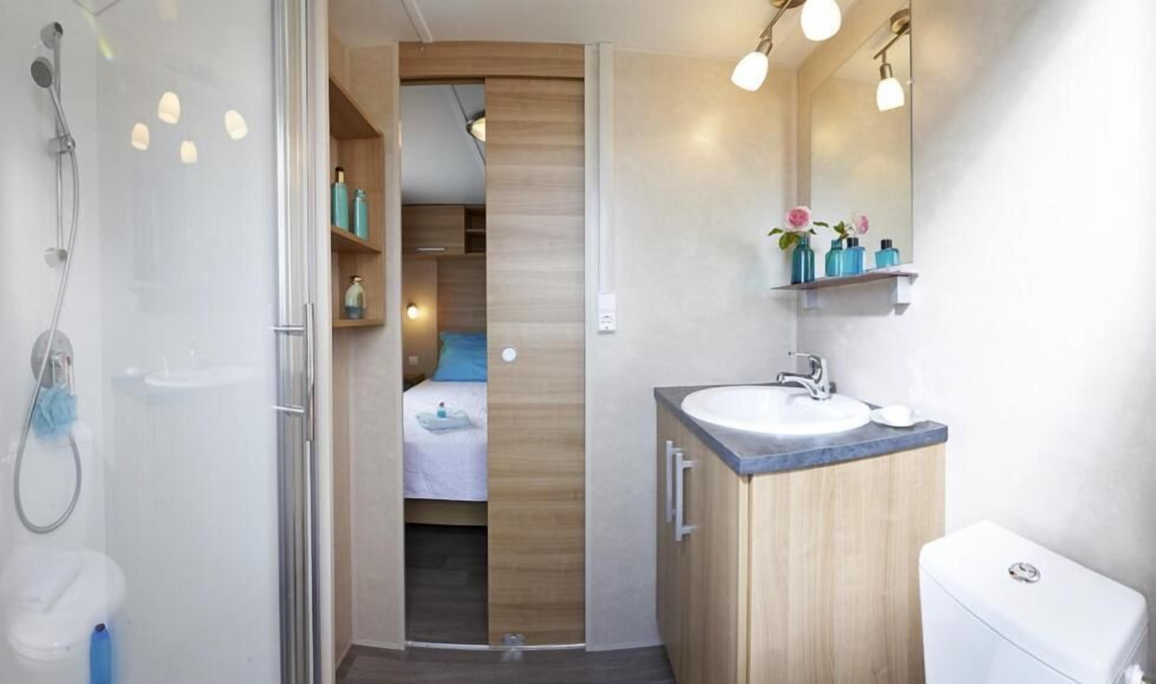 Un bagno moderno con doccia, lavandino e toilette. È presente un mobile bagno in legno con uno specchio e mensole sopra il lavandino.