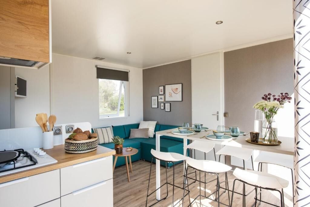 A modern kitchen with a dining area, a teal sofa, and a small table with chairs.