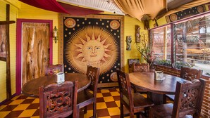 Een restaurantinterieur met houten tafels en stoelen, een grote zonsondergangsmural op de muur en een geruit vloertje.