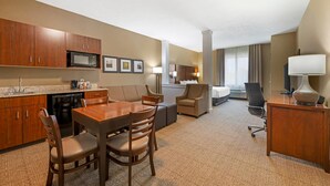 Une chambre d’hôtel équipée d’une kitchenette, d’un coin repas, d’un espace de vie avec un canapé et des fauteuils, ainsi que d’un bureau avec une lampe.